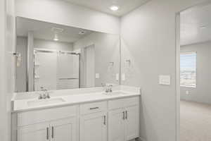 **DISLCAIMER** Interior package & colors may vary. Full bathroom with double vanity, a shower stall, and a textured ceiling