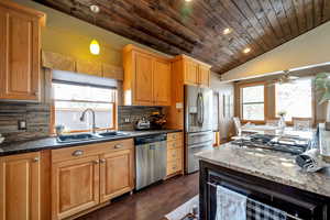 Kitchen with dark stone countertops, a vaulted wood ceiling, stainless steel appliances, pendant lighting, and dark wood-style floors