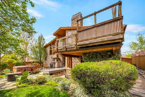 Rear view of property with a hot tub, a wooden deck, stone siding, a chimney, and a patio area