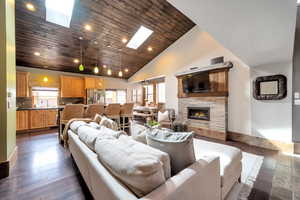 Living room with a vaulted wood ceiling, a skylight, dark wood-style floors, recessed lighting, and a stone fireplace