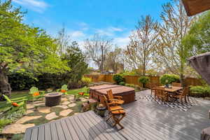 Wooden terrace featuring a fire pit, outdoor dining space, a patio, a hot tub, and a fenced backyard
