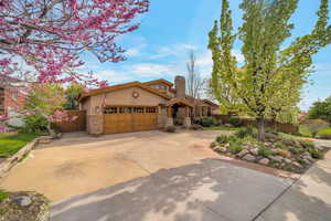 View of front facade featuring stucco siding, a garage, driveway, stone siding, and a chimney