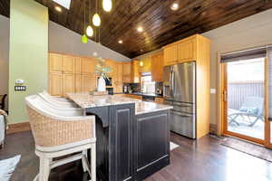 Kitchen featuring light stone counters, stainless steel appliances, hanging light fixtures, a breakfast bar, and a kitchen island
