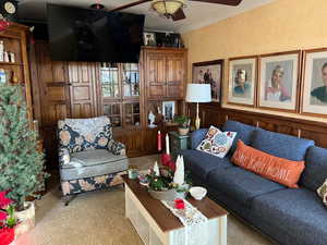 Living room featuring ornamental molding, carpet floors, a ceiling fan, and a textured ceiling