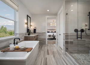 Full bath featuring tile walls, vanity, a stall shower, a soaking tub, and a chandelier