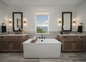 Full bath with tile walls, two vanities, and a soaking tub
