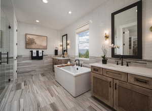 Bathroom featuring tile walls, a freestanding tub, two vanities, a shower stall, and recessed lighting