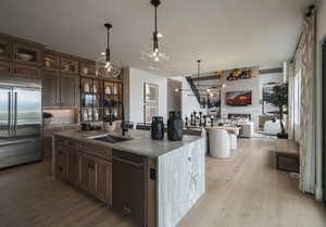 Kitchen featuring dark stone counters, stainless steel appliances, a large fireplace, light wood-type flooring, and pendant lighting