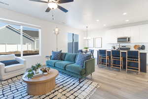 Living area with a ceiling fan, light wood-type flooring, and hanging lights