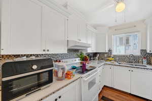 Kitchen with white range with electric stovetop, white cabinetry, and hardwood