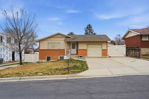 View of front facade featuring brick siding, driveways, a gate, an attached garage, and a shingled roof