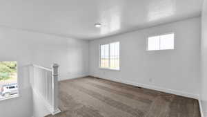 Carpeted spare room featuring a textured ceiling and baseboards