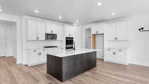 Two tone kitchen featuring a kitchen island with sink, light wood-type flooring, stainless steel appliances, light stone counters, and dual tone cabinets