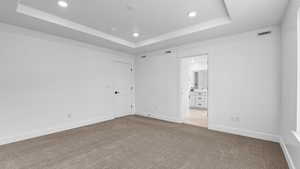 Unfurnished bedroom with recessed lighting, a raised ceiling, carpet floors, and ensuite bathroom