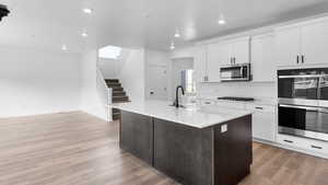 Kitchen featuring stainless steel appliances, light wood-style floors, a center island with sink, two tone color scheme, and light stone counters