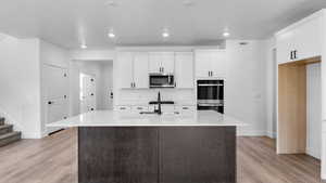 Dual tone kitchen with a center island with sink, two tone color scheme, light wood finished floors, stainless steel appliances, and light stone countertops