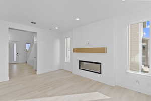Unfurnished living room with a glass covered fireplace, recessed lighting, and light wood-style flooring