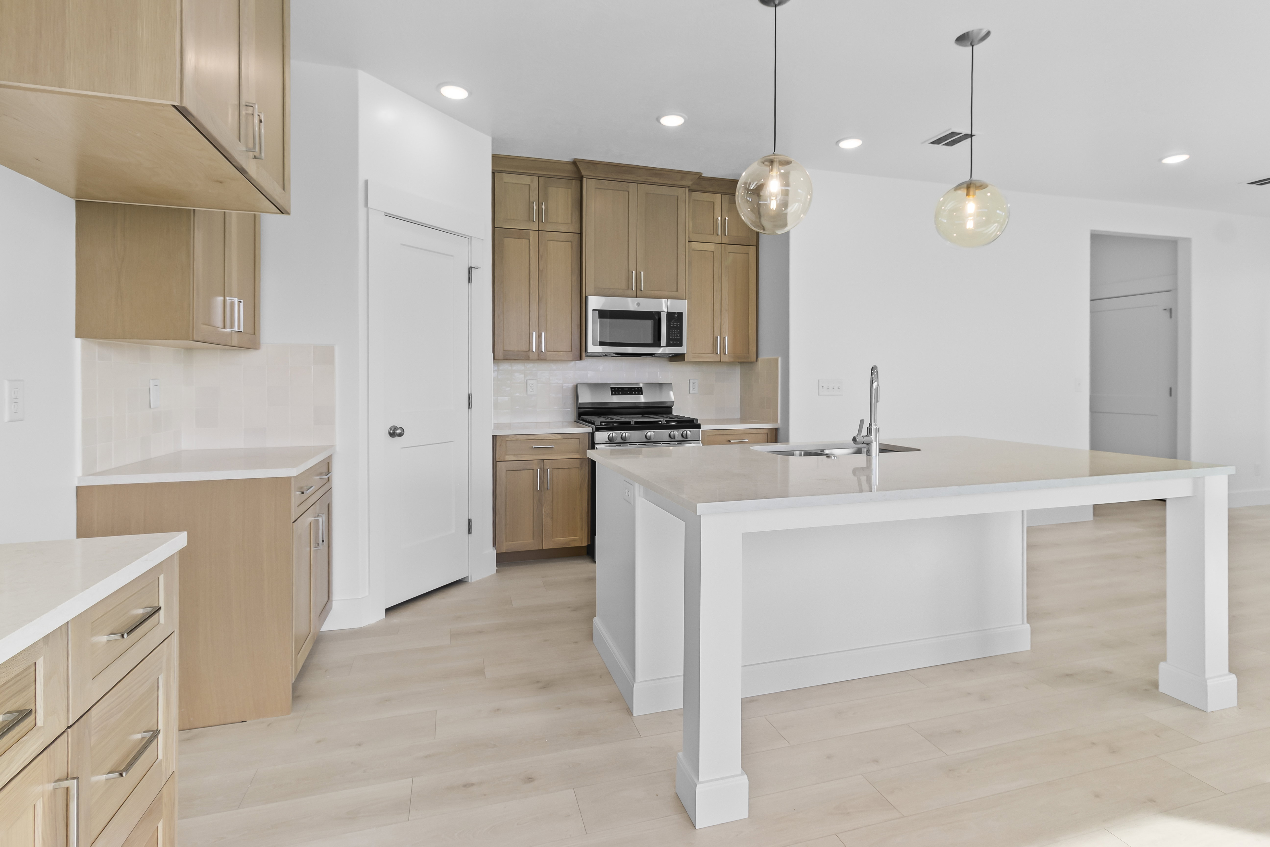 Kitchen with stainless steel appliances, light stone countertops, light wood-style floors, an island with sink, and pendant lighting