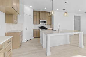 Kitchen with stainless steel appliances, light stone countertops, light wood-style floors, an island with sink, and pendant lighting