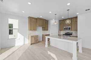 Kitchen featuring a kitchen bar, wood finish cabinets, stainless steel appliances, and light wood-style flooring