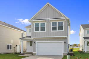 View of front of house featuring board and batten siding, a front lawn, a garage, and driveway