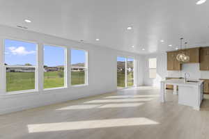 Kitchen with wood finish cabinetry, decorative light fixtures, light wood-type flooring, and open floor plan