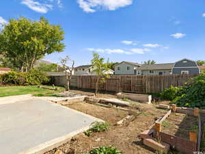 Fenced backyard featuring a vegetable garden, a residential view, and a patio area