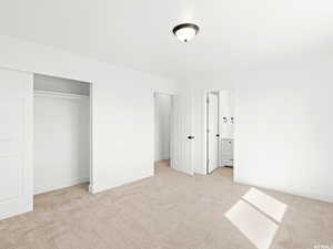 Unfurnished bedroom with light carpet, a closet, and ensuite bath
