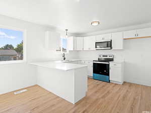 Kitchen with stainless steel appliances, a peninsula, light wood-style flooring, hanging light fixtures, and white cabinetry