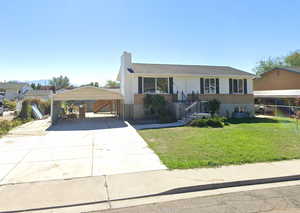 View of front of house featuring a detached carport, a front lawn, concrete driveway, a chimney, and brick siding