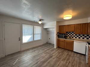 Kitchen featuring light countertops, wood finish cabinetry, white appliances, a textured ceiling, & laminate vinyl plank flooring.