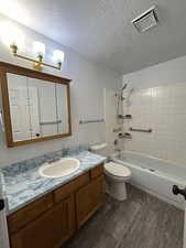Full bath featuring vanity, shower / tub combination, laminate vinyl plank flooring & a textured ceiling.