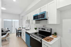Kitchen with stainless steel electric stove, white cabinetry, dishwasher, light wood-type flooring, and light stone countertops