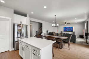 Kitchen with stainless steel refrigerator with ice dispenser, open floor plan, white cabinetry, light wood-style floors, and a center island