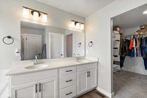 Full bath with double vanity, a spacious closet, and light carpet