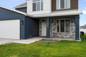Entrance to property featuring stone siding, a porch, a standing seam roof, a lawn, and an attached garage