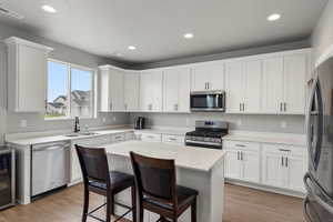 Kitchen with stainless steel appliances, white cabinets, light wood-style floors, a kitchen breakfast bar, and beverage cooler