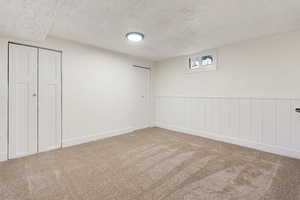 Unfurnished bedroom featuring a textured ceiling, carpet flooring, a wainscoted wall, and multiple closets