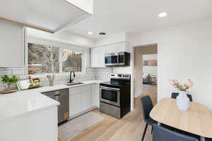 Kitchen with stainless steel appliances, white cabinets, light wood-style floors, light stone countertops, and recessed lighting