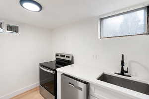 Kitchen with stainless steel appliances, healthy amount of natural light, light wood-type flooring, light stone countertops, and a textured wall