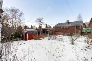 Snow covered rear of property with a shed, a patio, and brick siding