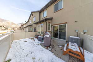 Snow covered rear of property with a fenced backyard, stucco siding, a patio, and a mountain view