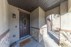 Property entrance with stone siding, stucco siding, and a porch