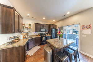 Kitchen with dark wood finish cabinets, black appliances, dark wood finished floors, recessed lighting, and a kitchen bar