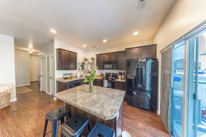 Kitchen featuring dark wood finish cabinetry, black appliances, dark wood-style flooring, a center island, and a breakfast bar