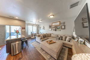 Living room featuring a textured ceiling, dark wood finished floors, and suspended lighting
