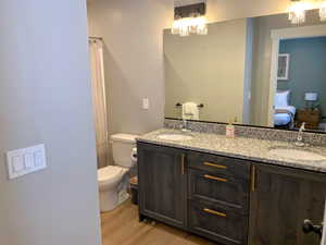 Ensuite bathroom featuring double vanity, light wood-type flooring, a shower with curtain, and hanging lights