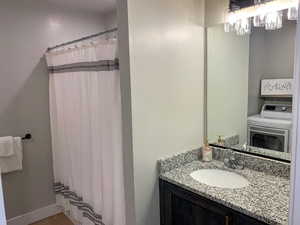 Full bath with a shower with curtain, washer / clothes dryer, vanity, and wood finished floors