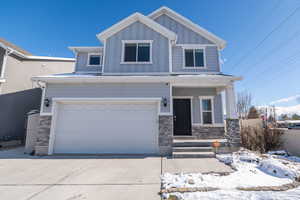 View of front of home with stone siding, a porch, an attached garage, and driveway
