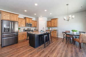 Kitchen with stainless steel appliances, light stone counters, a breakfast bar, a kitchen island with sink, and hanging lights